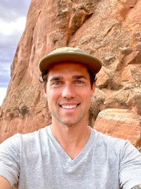 a man in a hat is taking a selfie in front of a rock formation